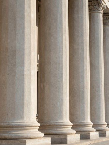 Close-up of classic stone columns of a courthouse, soft natural lateral afternoon light, clean architectural lines, minimalist composition.