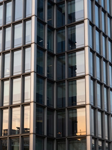 Symmetrical architectural shot of a modern corporate building facade with clean steel lines and warm golden sunset reflections on glass panels, editorial corporate style