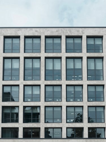 Straight-on architectural elevation of a modern commercial concrete and steel office building under bright overcast daylight, cool desaturated blue tones, sharp focus