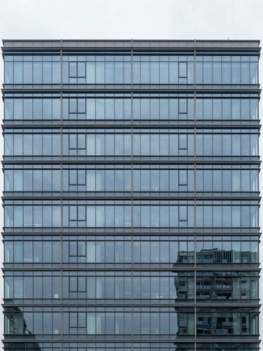 Straight-on architectural elevation of a modern commercial office building with clean glass facades, bright overcast daylight, cool desaturated slate tones, sharp focus, 35mm lens