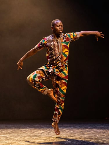 Close wide shot of a contemporary African dancer mid-leap on a dimly lit stage, spotlight catching the folds of a richly textured kente-patterned costume, dark background, golden hour warmth flooding from stage left