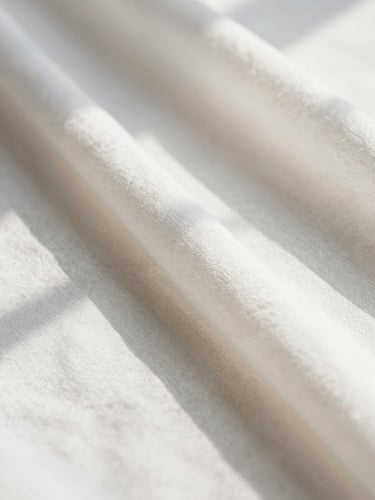 Macro close-up of soft white linen fabric being meticulously steamed, warm golden sunlight casting gentle shadows, shallow depth of field