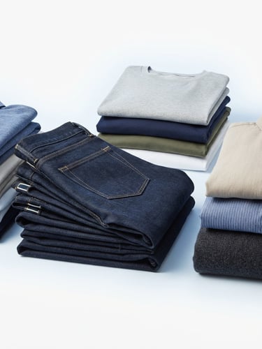 Bright commercial product photography of neatly folded stacks of shirts and jeans, crisp studio lighting, clean white background, 50mm