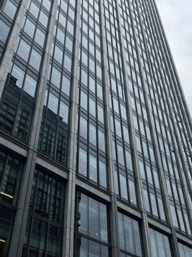 Cool architectural photography of a modern glass and steel skyscraper facade, sharp overcast daylight, desaturated blues and slate tones, wide-angle lens, high-contrast corporate realism.