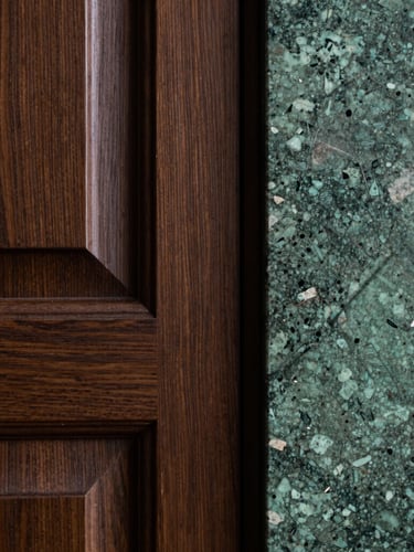 A close-up vertical shot of custom dark oak joinery meeting a rough-hewn green quartzite slab, dramatic side lighting highlighting the rich textures and recessed detailing.