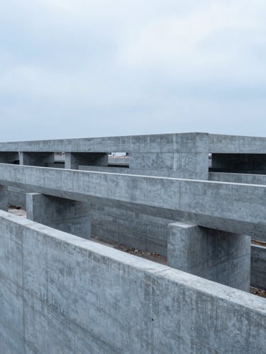 Wide environmental shot of a massive concrete infrastructure project under cool overcast daylight, desaturated blue and slate tones, high-contrast composition.