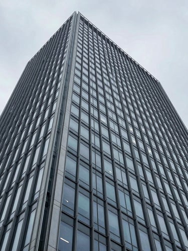 Wide-angle architectural photograph of a modern steel and glass skyscraper facade, sharp overcast daylight, cool desaturated blue and slate tones, high-contrast structural composition