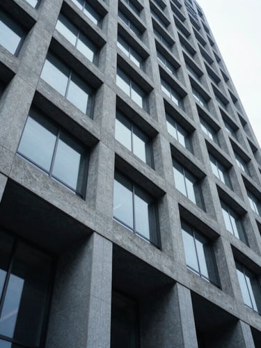 Low-angle architectural shot of a modern concrete and steel corporate skyscraper facade under cool overcast daylight, desaturated blue tones, sharp geometric lines