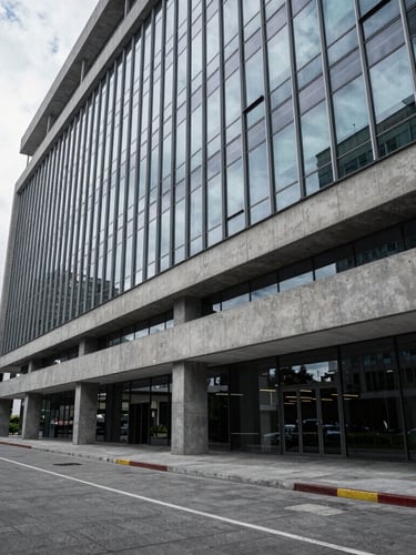 Wide architectural view of a modern corporate office in Quito, cool daylight reflecting on polished concrete and glass, structured and professional setting, generous negative space on the left.