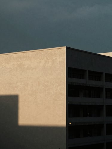 Quiet urban landscape of Jakarta at dusk, soft overcast light, dramatic shadows, warm cream and deep blue tones, minimalist composition