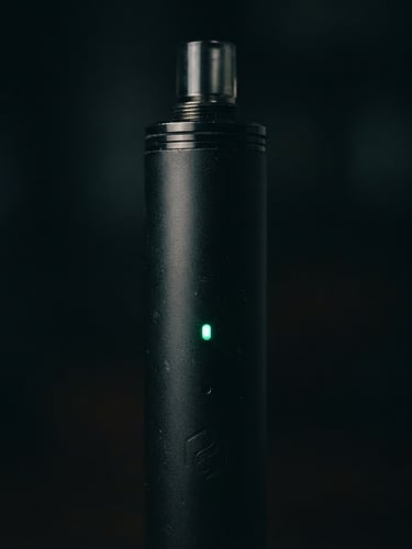 Sleek close-up of a matte black vape device with a subtle emerald green light glowing on its indicator, dark low-key lighting, highly detailed macro shot, 50mm lens