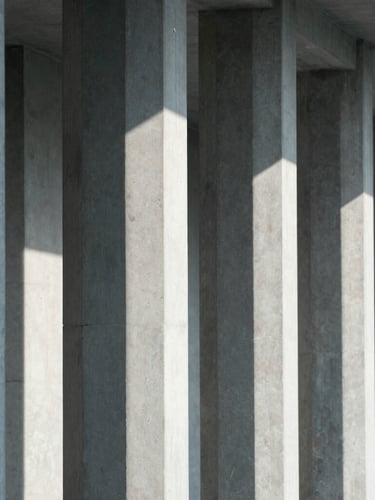 An architectural close-up of clean concrete columns and sharp, directional shadows cast by cool, diffused daylight, emphasizing structural depth and minimalist design.