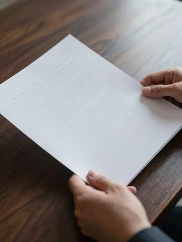 Close-up of hands holding a heavy textured paper document over a dark wooden desk, soft natural side lighting, elegant and professional atmosphere.