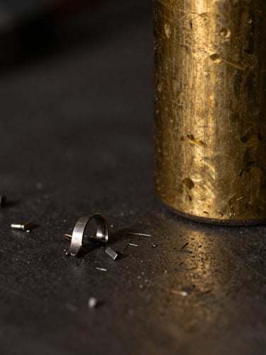 Macro detail of metal shavings on a dark workbench next to a heavy, raw brass cylinder, dramatic low-key side-lighting.