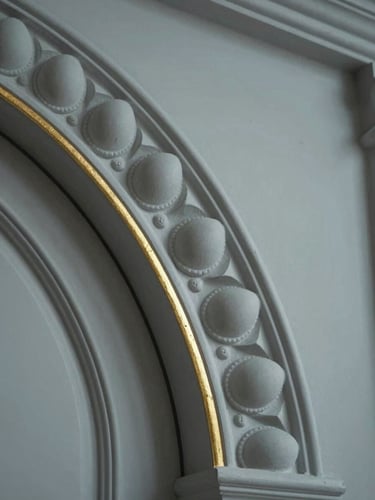 Extreme close-up of a classical door architrave detail — hand-cut plaster egg-and-dart molding, matte finish, a thin gold-leaf line at the reveal edge, cool even studio light, no depth of field blur