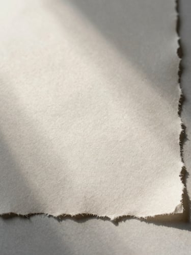 A close-up of textured handmade paper with raw deckled edges, soft morning mist light casting gentle shadows across the surface, minimalist composition.