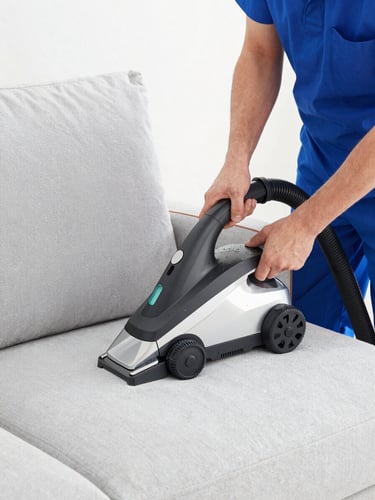 A professional upholstery cleaning technician in a clean uniform using a high-tech extraction machine on a light gray sofa, bright daylight, water droplets visible