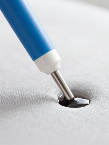 Macro photograph of a professional extraction cleaning nozzle pulling dark water out of a light grey fabric sofa, bright high-key daylight, clean blue and white tones, sharp focus.