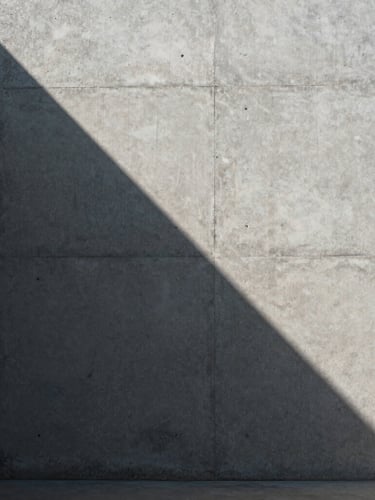 A sharp shaft of morning light cutting across a minimalist concrete wall, casting a crisp geometric shadow, architectural, sober, raw texture.