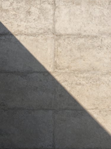 Perfect vertical alignment of a raw concrete wall, a sharp triangular shadow casting across its textured surface, warm natural afternoon light, minimalist composition, 3:4 portrait aspect.