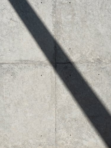 Perfect vertical shot of raw concrete wall meeting a sharp shadow line under harsh tropical sunlight, architectural abstraction, minimalist framing