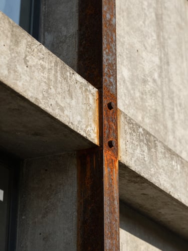 Macro close-up of raw concrete and rusted steel joint on a modernist facade, geometric lines, high-contrast shadow, warm afternoon sunlight.