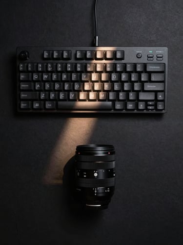 Overhead flat-lay of a dark studio keyboard and audio interface on a matte black surface, a single narrow beam of light cutting across the keys from the left, deep shadow on all sides, no people, no color