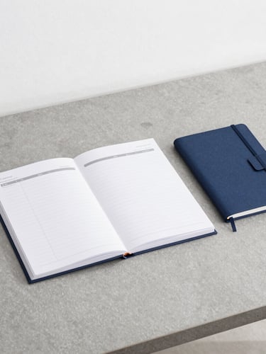 An organized minimalist workspace with a slate gray desk, a structured planner, a notebook, and clean architectural lines under bright neutral daylight