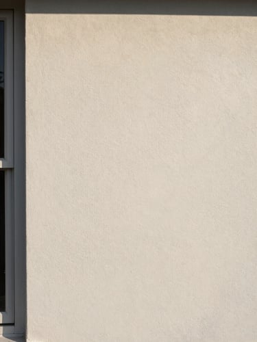 Close-up portrait-orientation photograph of a freshly painted residential wall in soft north-facing daylight, smooth paint surface revealing subtle tonal variation, a single window frame edge visible at far left, no furniture or people, surface quality as sole subject
