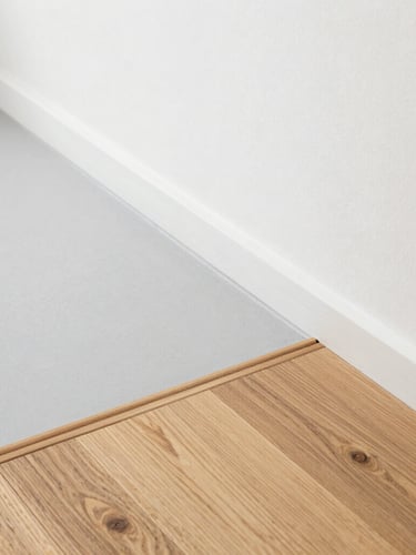 Architectural close-up, clean transition of oak wood flooring meeting a seamless light gray microcement floor, bright natural daylight, 35mm