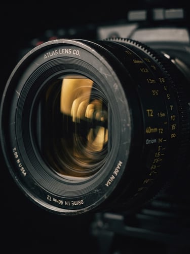 Extreme close-up of a high-end anamorphic camera lens, dramatic low-key lighting, deep shadows, gold reflections on the glass, rich 35mm film grain, cinematic atmosphere