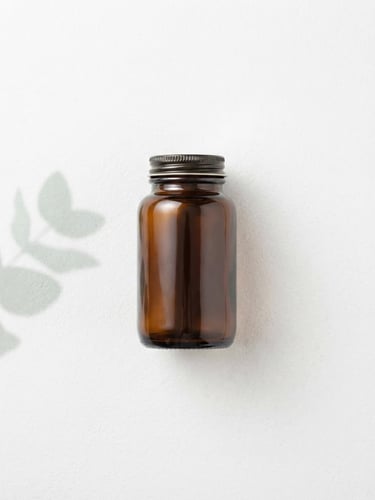 Overhead flat lay of single amber glass supplement bottle resting on a sterile white stone surface, clean studio lighting, soft mint green botanical leaf shadow