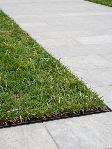 A crisp lawn edge meeting a clean stone driveway, showing a perfectly routed drainage and sub-surface irrigation installation under overcast coastal light.