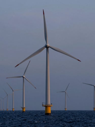An offshore wind array shot from a dramatic low angle at dusk, massive turbines rising from deep navy waters under a steel-gray sky.