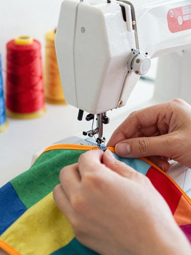 Close-up of hands carefully sewing a colorful pet garment with a sewing machine in a bright workshop, soft natural daylight, spools of bright thread in the background, 35mm