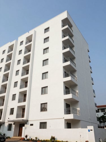 Wide environmental shot of a modern residential apartment building exterior in Andhra Pradesh, photographed in bright morning daylight from street level, clean white facade with balconies visible, open sky above, no people