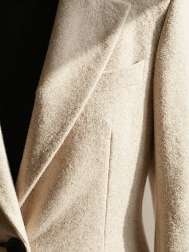 Close-up detail of high-quality beige wool fabric and structured black tailoring, warm window light casting soft shadows, elegant composition, minimalist editorial style