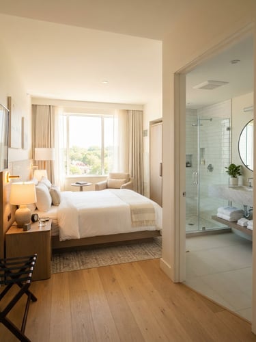 Bright interior photography of a spotless hotel room with crisp white linens, clean modern bathroom visible, natural daylight, warm inviting tones, realistic