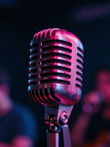 Moody close-up of a vintage microphone under dramatic magenta rim lighting, deep shadows, 35mm film grain, abstract concert aesthetic.