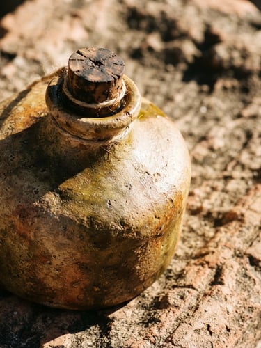 Extreme close-up of a raw ceramic bottle of olive oil on a rough terracotta stone surface, harsh Mediterranean sunlight, deep shadows, 35mm film