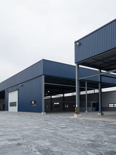 Wide environmental shot of a modern clean industrial logistics facility with structured steel architecture under bright overcast daylight, cool slate tones, sharp focus, 35mm lens