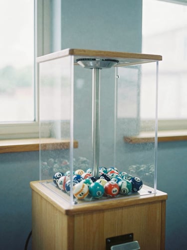 A physical lottery draw machine with a transparent acrylic chamber and numbered balls spinning inside, bright natural daylight from high windows, honest editorial 35mm photography