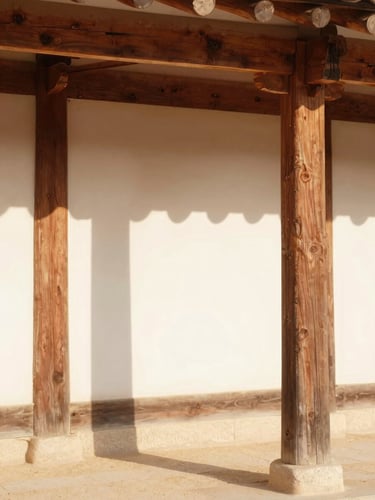 Warm editorial photograph of sunlit traditional Korean Hanok wooden pillars casting soft shadows on a clean minimalist plaster wall, Mediterranean light, 35mm