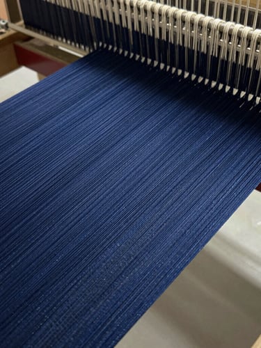 Macro close-up of deep indigo warp threads stretched tightly on a modern industrial loom, natural workshop light highlighting thread density and texture.