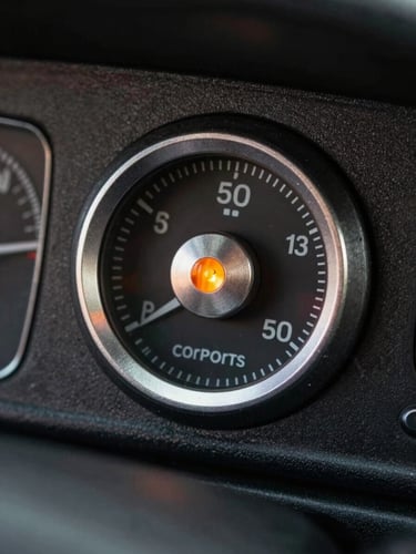 Macro close-up portrait of a physical vintage car instrument panel, focusing on a knurled metal dial and a glowing orange indicator light, sharp studio lighting, dark metallic textures