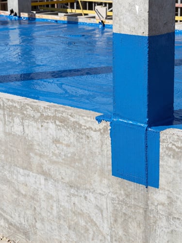 Industrial construction site in India, close-up of heavy-duty blue polyurethane waterproofing coating being applied to a thick concrete foundation wall, bright daylight, professional architectural photography