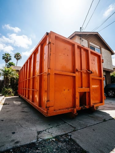 High-contrast industrial photography of a clean, safety-orange roll-off dumpster positioned on a residential driveway in Long Beach, bright midday sun, low-angle heroic shot, portrait aspect, showing clear scale.