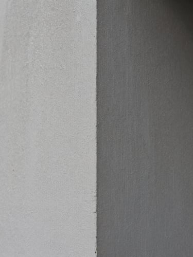 Crisp architectural photography, tight macro shot of raw plaster texture meeting a sharp corner, natural overcast daylight, desaturated slate tones, 35mm lens.