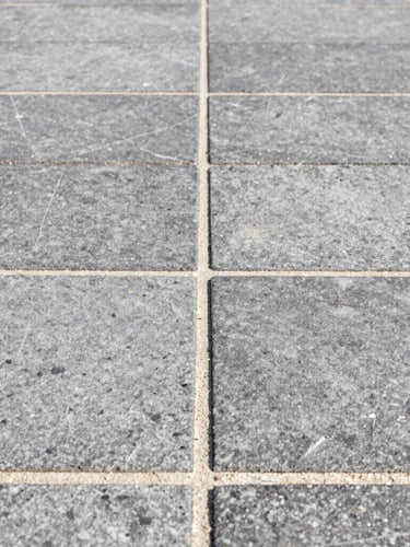 Close-up macro architectural photograph of perfectly aligned gray stone paver joints, clean stabilized sand lines, bright midday sun highlighting the texture