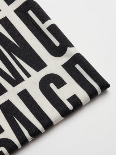 Overhead flat-lay of a custom-designed T-shirt on a clean off-white surface, bold graphic print visible, crisp studio strobe lighting, fabric texture sharp in frame, no props or distractions